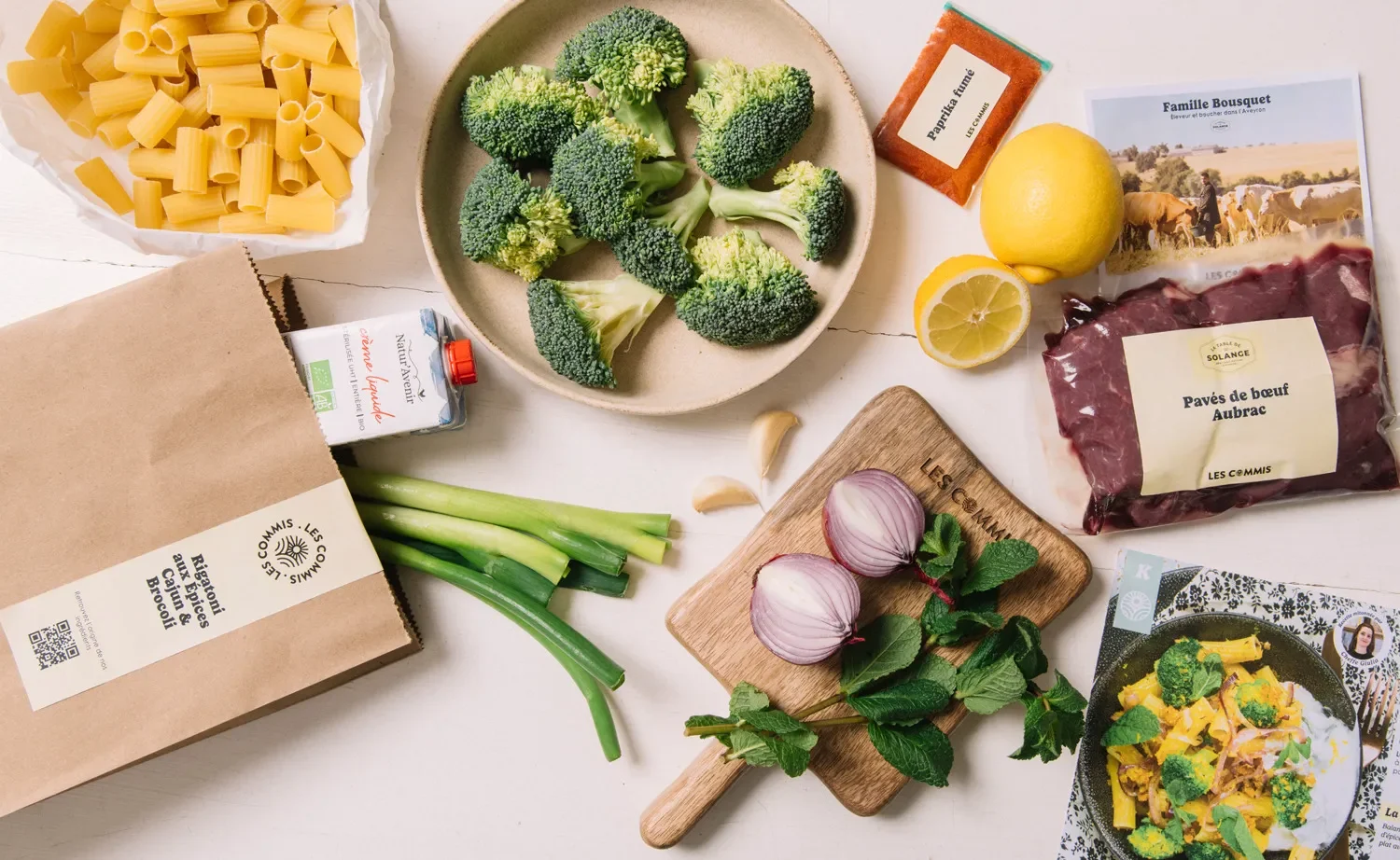 Les ingrédients frais d'une recette Les Commis disposés à plat : pâtes, brocoli, viande, herbes, sachet de la marque