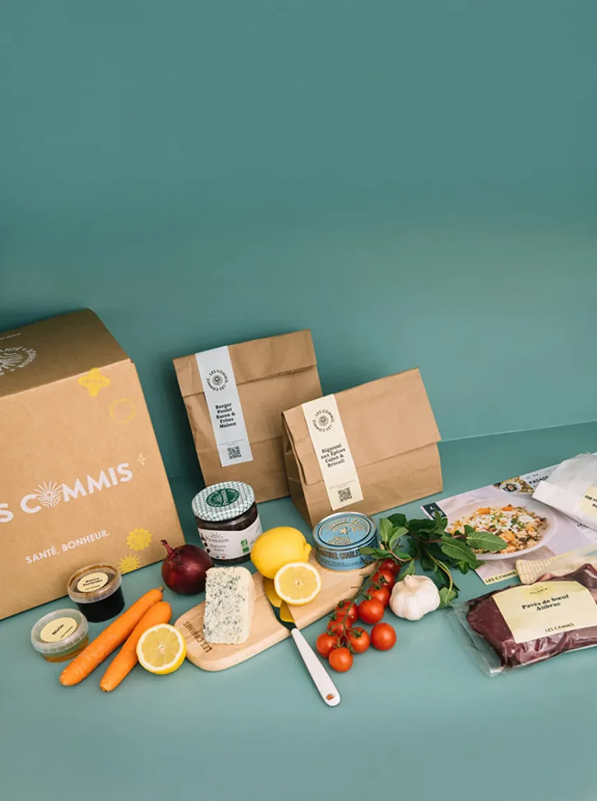 Le carton Les Commis entouré d'ingrédients frais : légumes, viande, fromage, fiches recettes