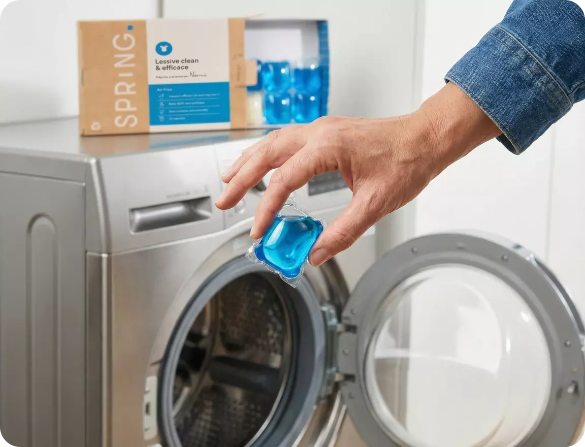 Une main insère une capsule de lessive Spring dans une machine à laver ouverte